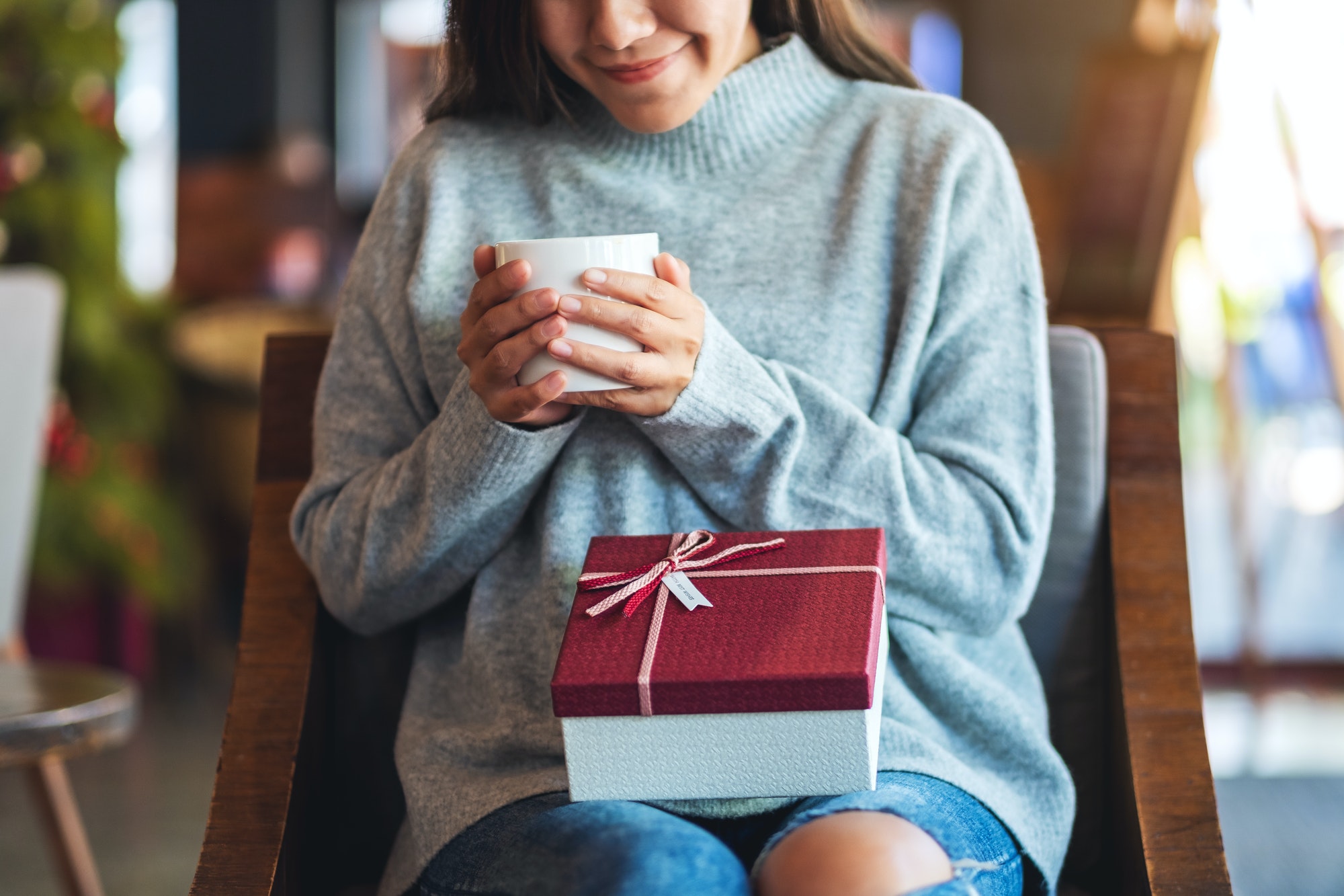 Closeup image of a beautiful young woman holding a gift box while drinking coffee