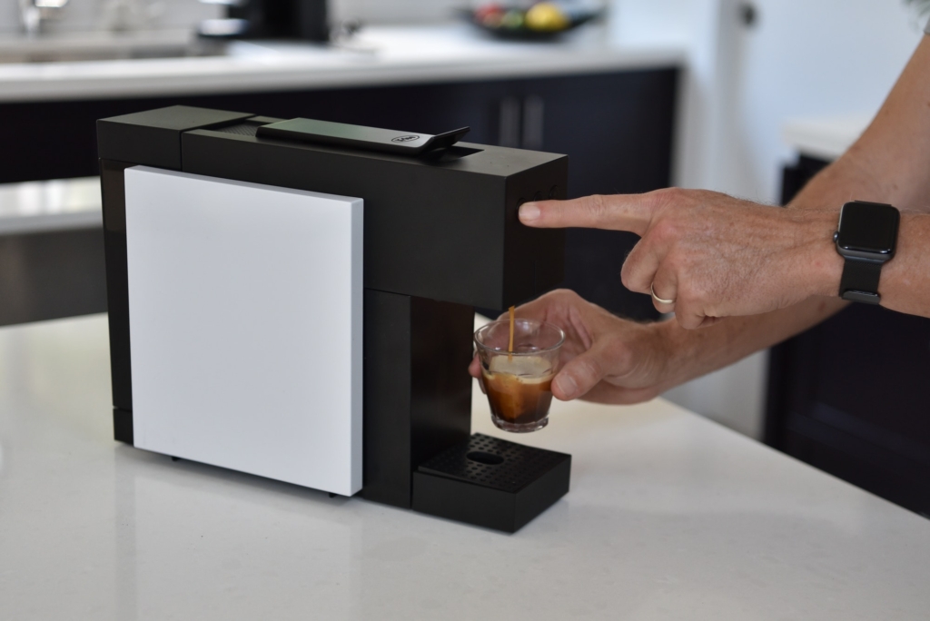 Making an expresso coffee in a pod coffee machine . A man pushes the button to make the coffee