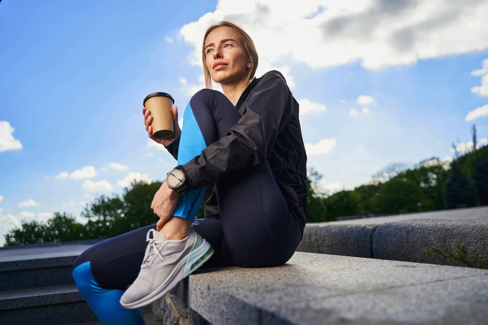 Calm sporty woman having cup of coffee outdoors