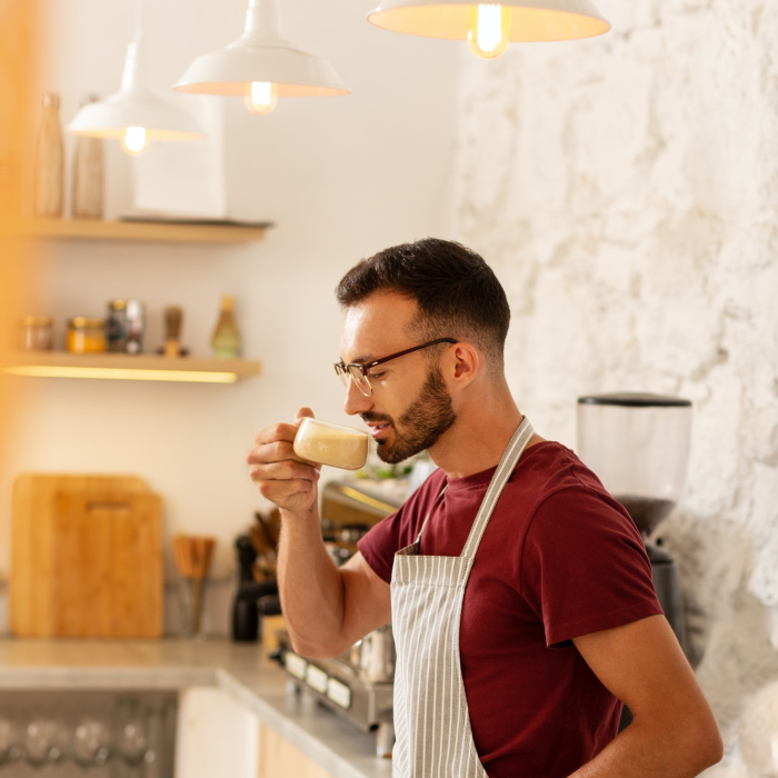 Bearded man owning coffee room standing and drinking coffee
