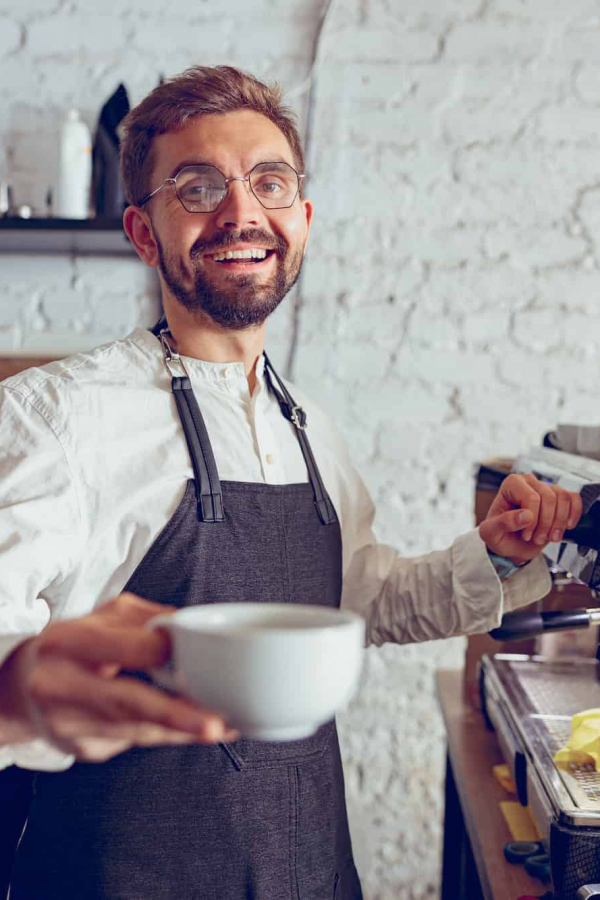 Cheerful male barista offering coffee in cafe
